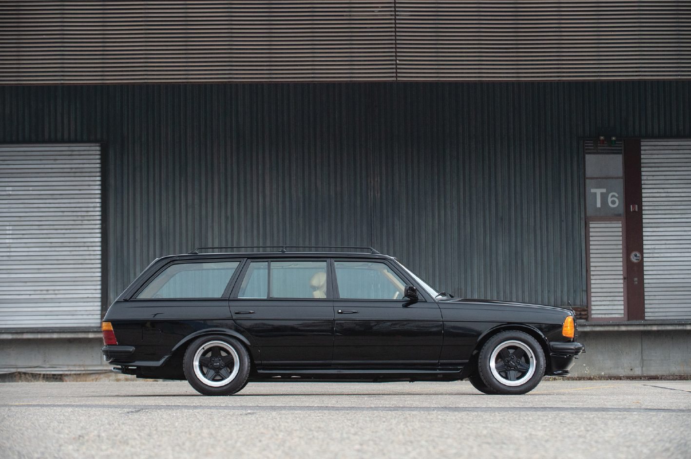 A black 1979 Mercedes-Benz 500TE AMG wagon parked in front of corrugated steel loading-dock shutters.
